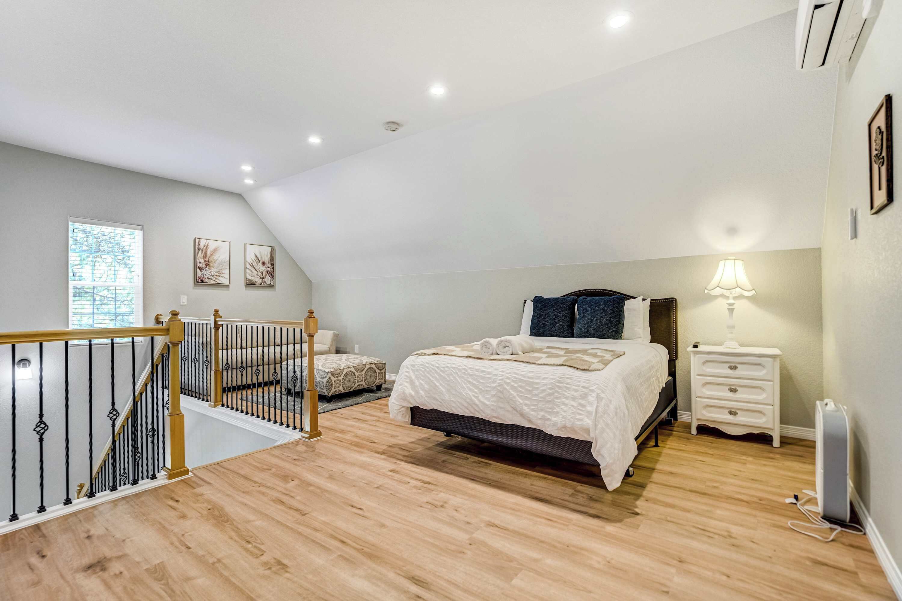 Un dormitorio con cama, mesitas de noche, lámpara, ventana y una escalera.