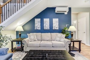 A living room with a grey sofa, two side tables with lamps, a black rug, and a staircase with a white railing.