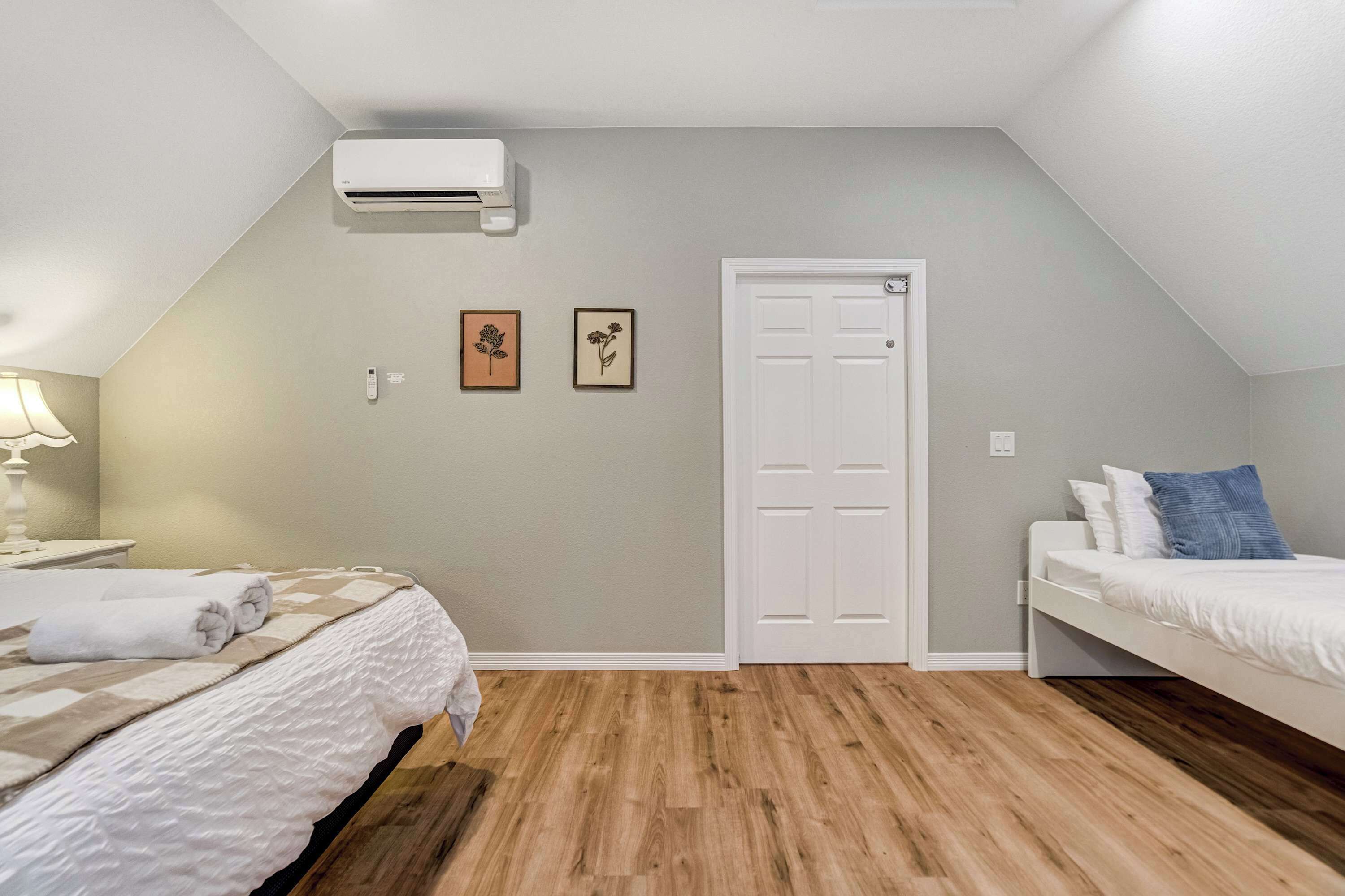 Une chambre avec un plafond en pente, un climatiseur blanc, une porte et deux tableaux encadrés accrochés au mur.