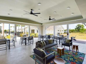 Amplo espaço interno com ventiladores de teto, mesas, cadeiras e um tapete colorido.