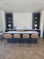 Una cocina moderna con una isla central, taburetes de bar y estanterías empotradas.
