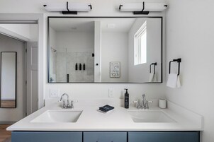 Un baño moderno con dos lavamanos, un espejo grande y una ducha que se ve en el reflejo.