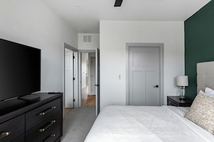 Un dormitorio con cama, cómoda, televisor, mesita de noche, lámpara y puerta.