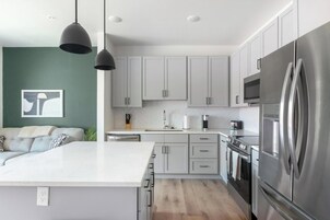 Una cocina moderna con gabinetes grises, un refrigerador de acero inoxidable e iluminación colgante.