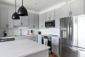 A modern kitchen with grey cabinets, stainless steel appliances, a central island, and pendant lighting. - Landing Modern 2bd, Pool, Clubhouse (Edmond)