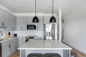 A modern kitchen with grey cabinets, a stainless steel refrigerator, a microwave, and a central island with two pendant lights.