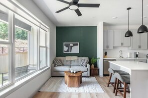 Una cocina moderna con armarios blancos, un comedor con un taburete de bar y una sala de estar con sofá y mesa de centro.