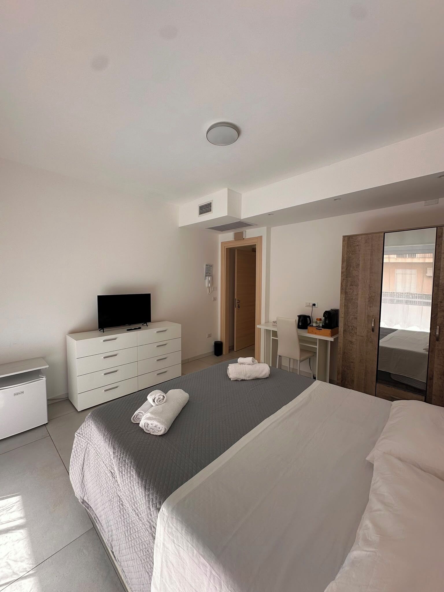 Ein Hotelzimmer mit einem Bett, einem Fernseher, einem Schminktischchen, einem Schreibtisch und einem Kleiderschrank.