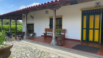 Un espacio al aire libre techado con piso de piedra, bancos y plantas en macetas.