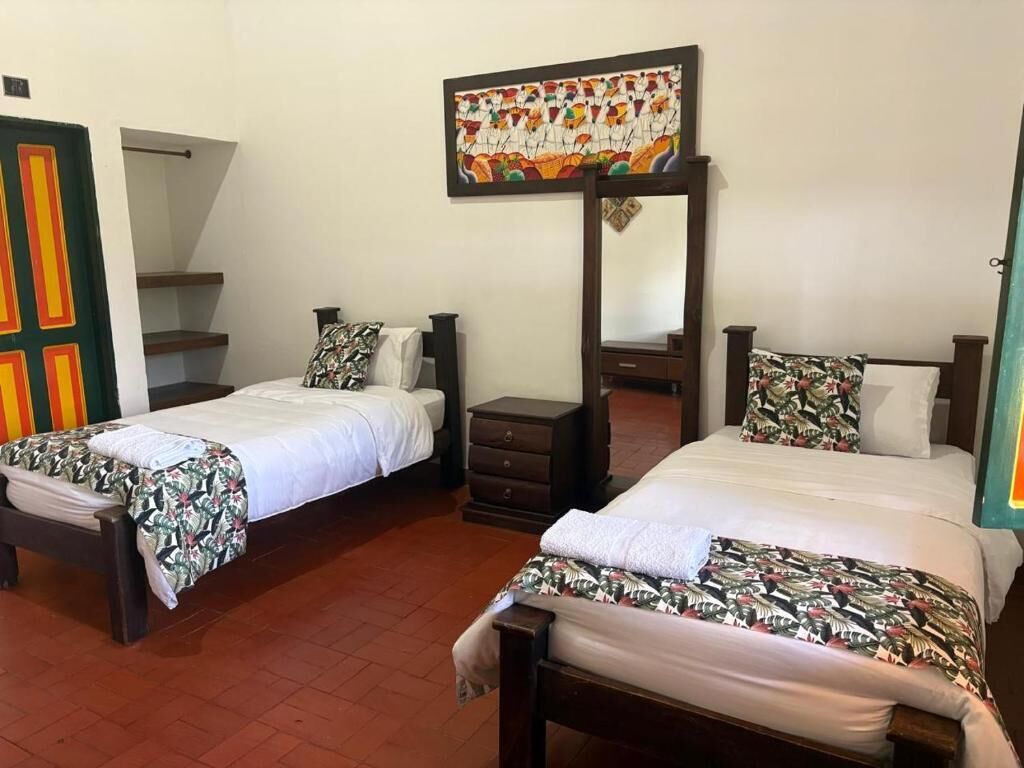 Una habitación de hotel con dos camas, un armario, un espejo y una obra de arte colorida en la pared.