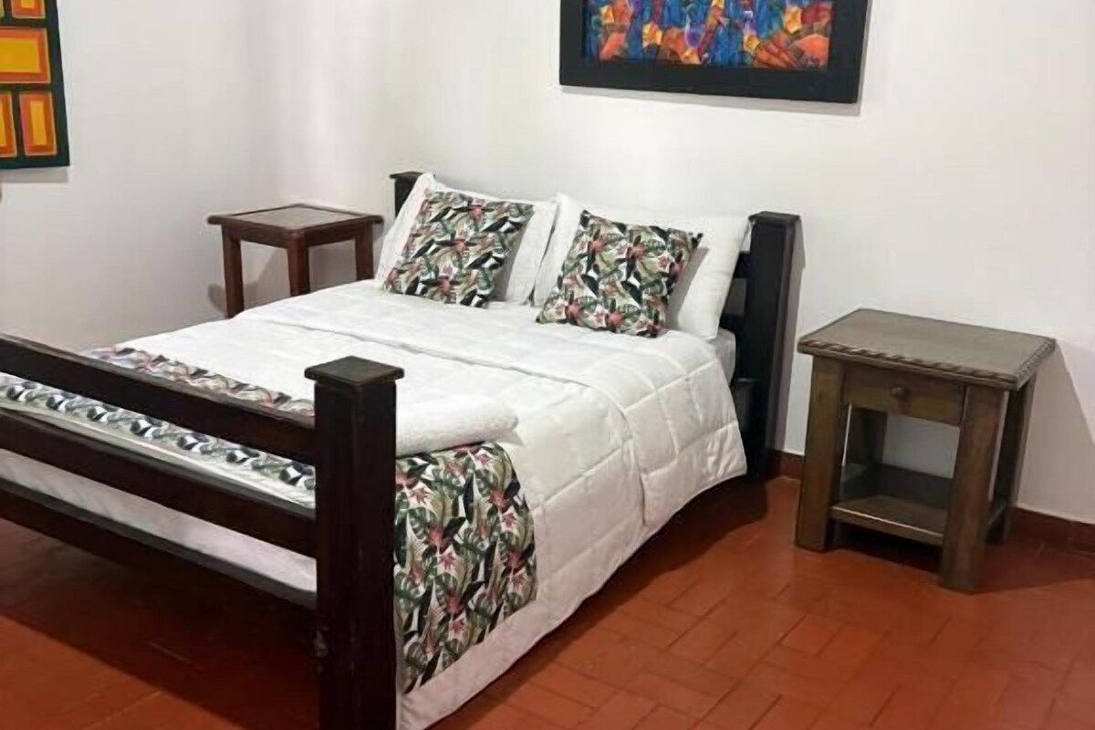 Ein Schlafzimmer mit einem Bett, zwei Nachttischen, einem Wandbild und einem Fliesenboden.