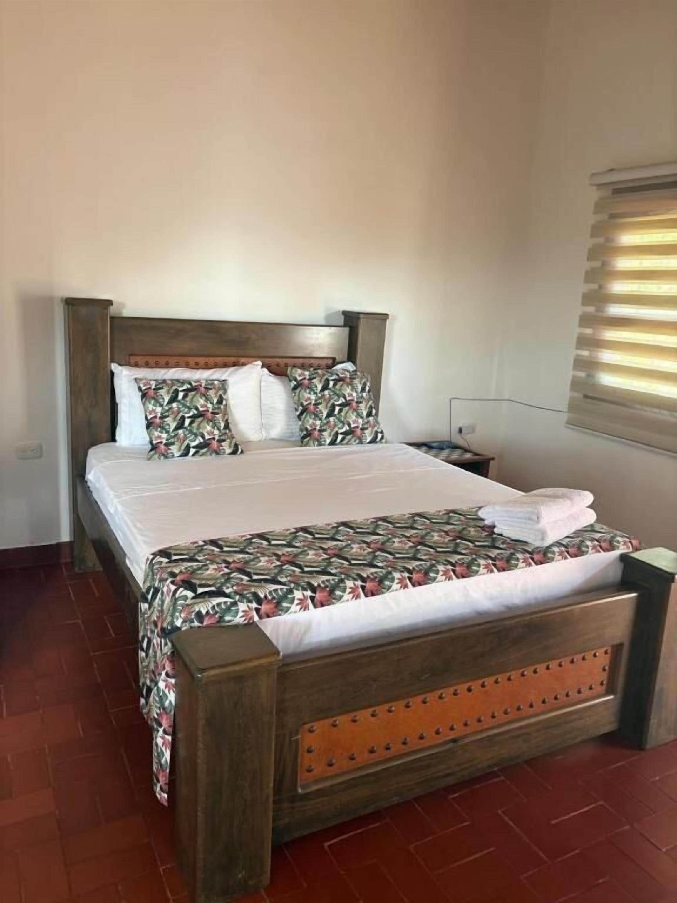 Une chambre à coucher avec un lit en bois, une table de chevet, une lampe et une fenêtre avec des stores.