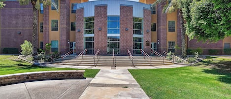 A multi-story building with a central atrium, surrounded by a well-maintained lawn and palm trees.