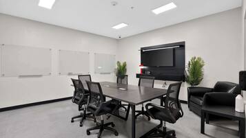 A conference room with a long table, six chairs, a flat-screen TV, and two potted plants.