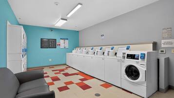 A laundry facility with multiple washing machines, a seating area, and informational posters on the walls.