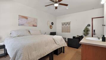 A bedroom with a bed, a desk, a chair, a vanity with a mirror, and a ceiling fan.