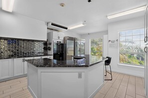 A modern kitchen with white cabinetry, a central island, and a view of greenery outside. - The Nest | Cozy Comfort near DT Tempe and UAT (Tempe)