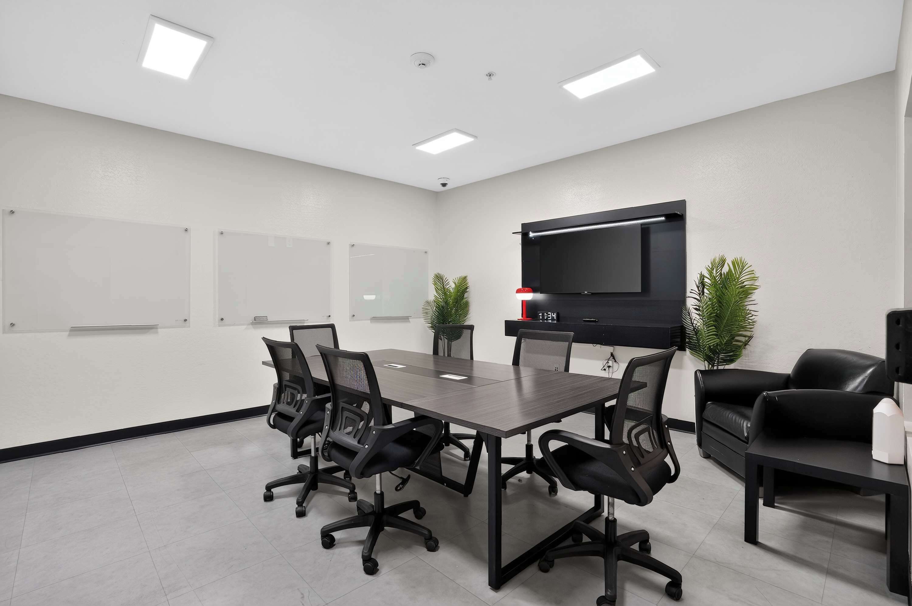 A conference room with a long table, six chairs, a flat-screen TV, and two potted plants.