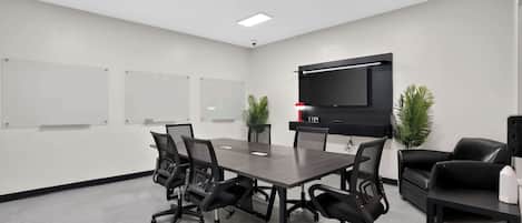 Une salle de conférence avec une longue table, six chaises, un téléviseur à écran plat et deux plantes en pot.