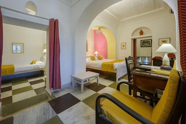 A hotel room with two beds, a small table, a chair, and a desk with a lamp.