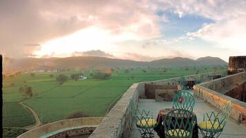 Una terrazza con vista su un paesaggio verde e colline lontane, con un tavolo e sedie rotonde.