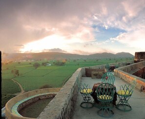 A terrace with a view of a green landscape and distant hills, featuring a round table and chairs.