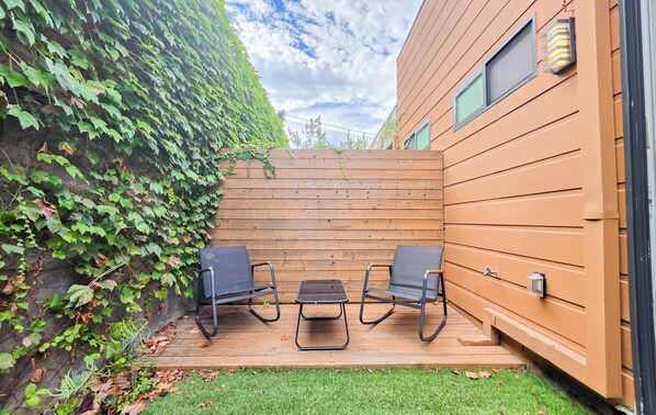 A patio with two chairs and a table, surrounded by a wooden fence and a wall covered in ivy.