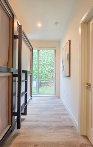 A hallway with a wooden floor, a sliding glass door leading to a garden, and a framed picture on the wall.