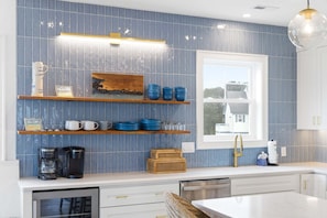 A kitchen with blue tiles, wooden shelves, and a window. - Reelin 22: Canalfront, Boat Dock, Pirate's Cove Community Amenities (Manteo)