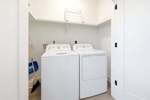 A laundry room with two white washing machines and a blue mop leaning against the wall. - Reelin 22: Canalfront, Boat Dock, Pirate's Cove Community Amenities (Manteo)