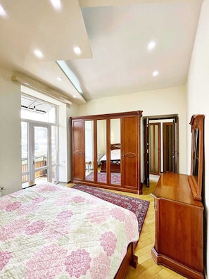 Un dormitorio con una cama grande, un armario y un espejo. Hay una ventana que proporciona luz natural.