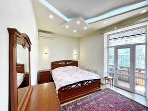 Una camera da letto con un letto di legno, comodini, uno specchio, un termosifone e un'ampia finestra con vista.