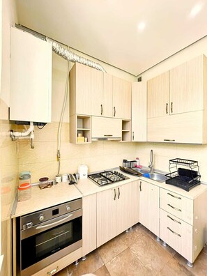 A kitchen with light wooden cabinets, a gas stove, an oven, and a sink. - Bright & Cozy Yerevan Apartment with City View Near City Center & Self Check-in (Yerevan)