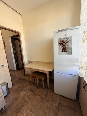 Una cocina con refrigerador, una mesa de madera y un banco.
