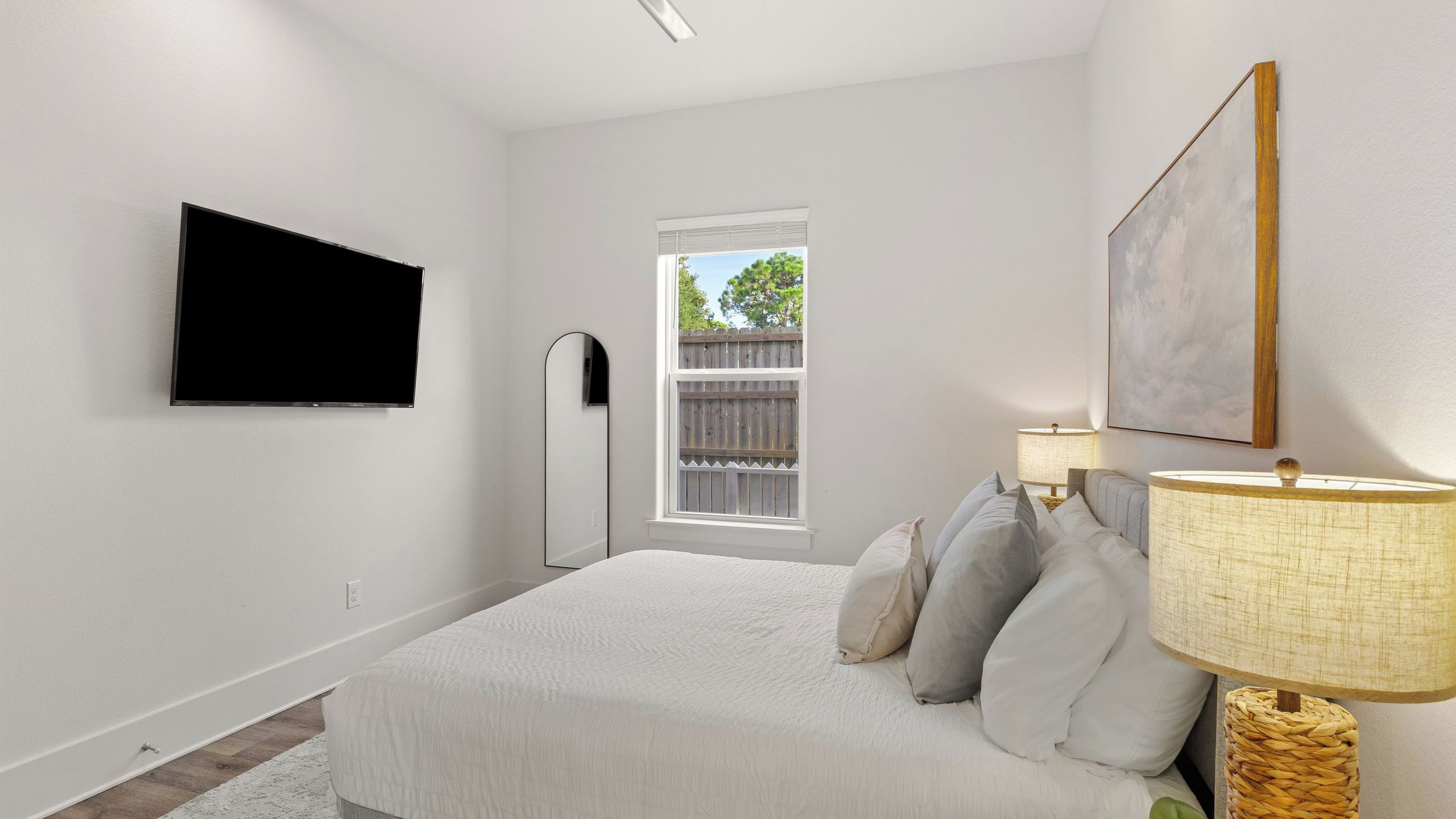 A bedroom with a bed, a TV mounted on the wall, a window, and a painting.