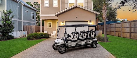 Un carrito de golf estacionado en una entrada de casa, con una vivienda al fondo.
