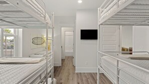 Ein Zimmer mit Etagenbetten, einem Wand-Fernseher und einer Tür zu einem weiteren Raum.