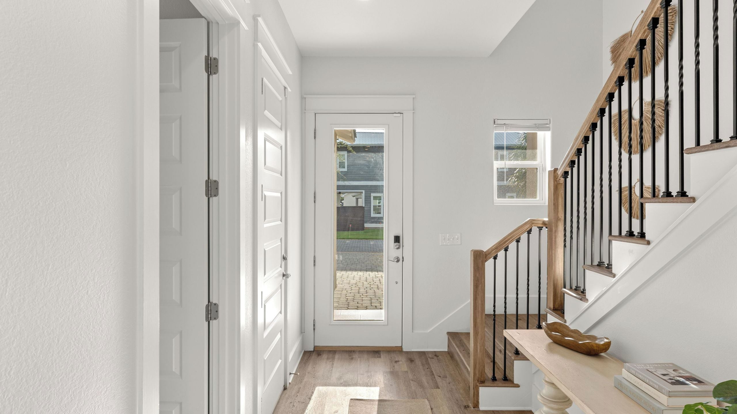 Un couloir avec une porte blanche, un escalier avec des marches en bois et des balustrades noires, et une petite fenêtre.