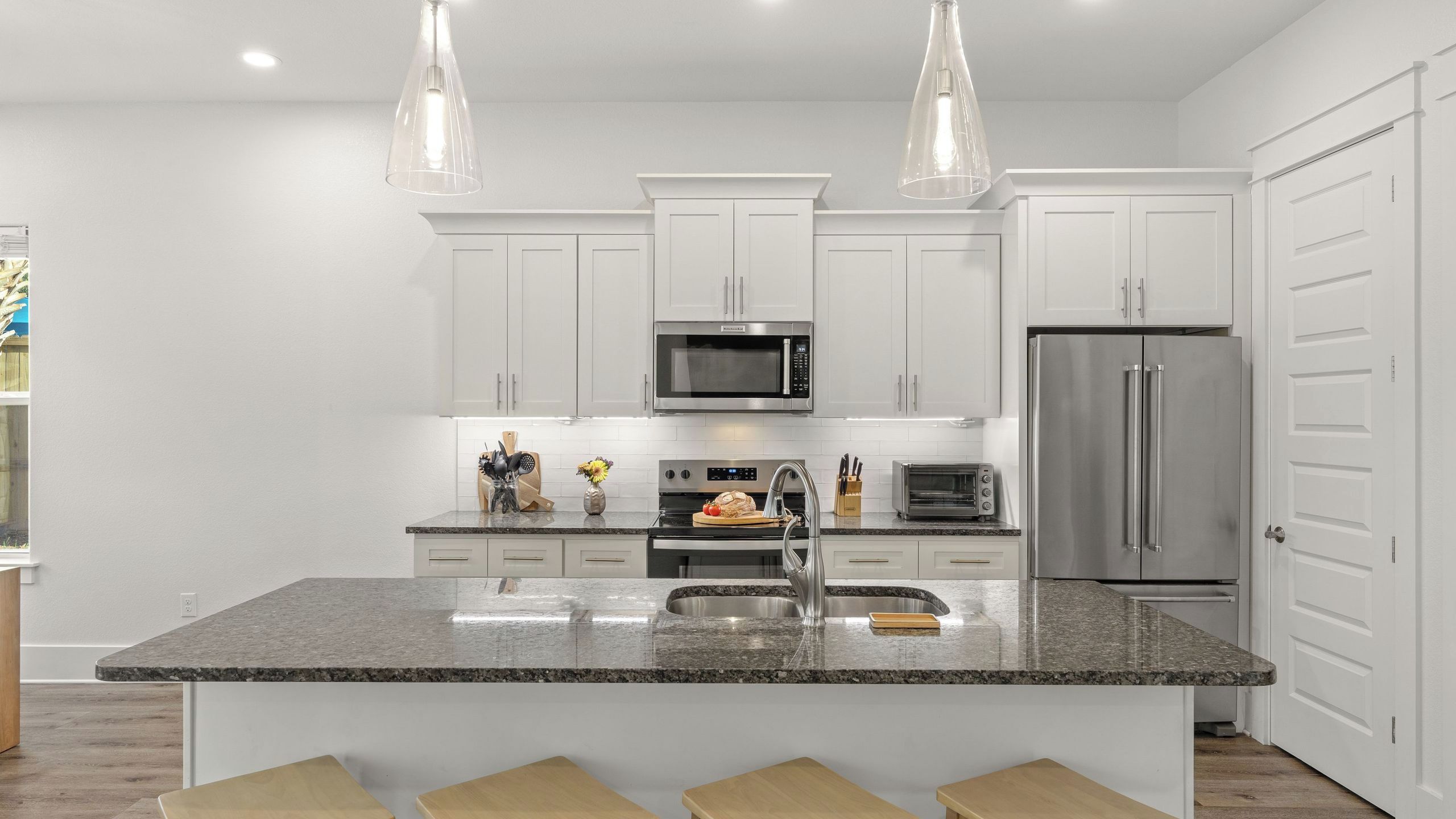 A modern kitchen with white cabinets, a stainless steel refrigerator, a microwave, and a large island with a sink.