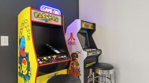 Zwei Spielautomaten, einer mit der Aufschrift 'PAC-MAN' und der andere 'CENTIPEDE', mit einem Hocker vor dem 'CENTIPEDE'-Automaten.