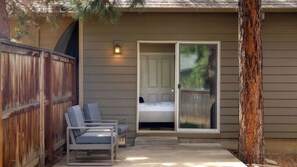 A covered outdoor seating area with two chairs and a table, a sliding glass door leading to a bedroom, and a wooden fence. - Hollygrape Pedal & Pine Hideaway by Avantstay Bend Hideaway Deck + Near Mt. Bachelor + Breweries (Bend)