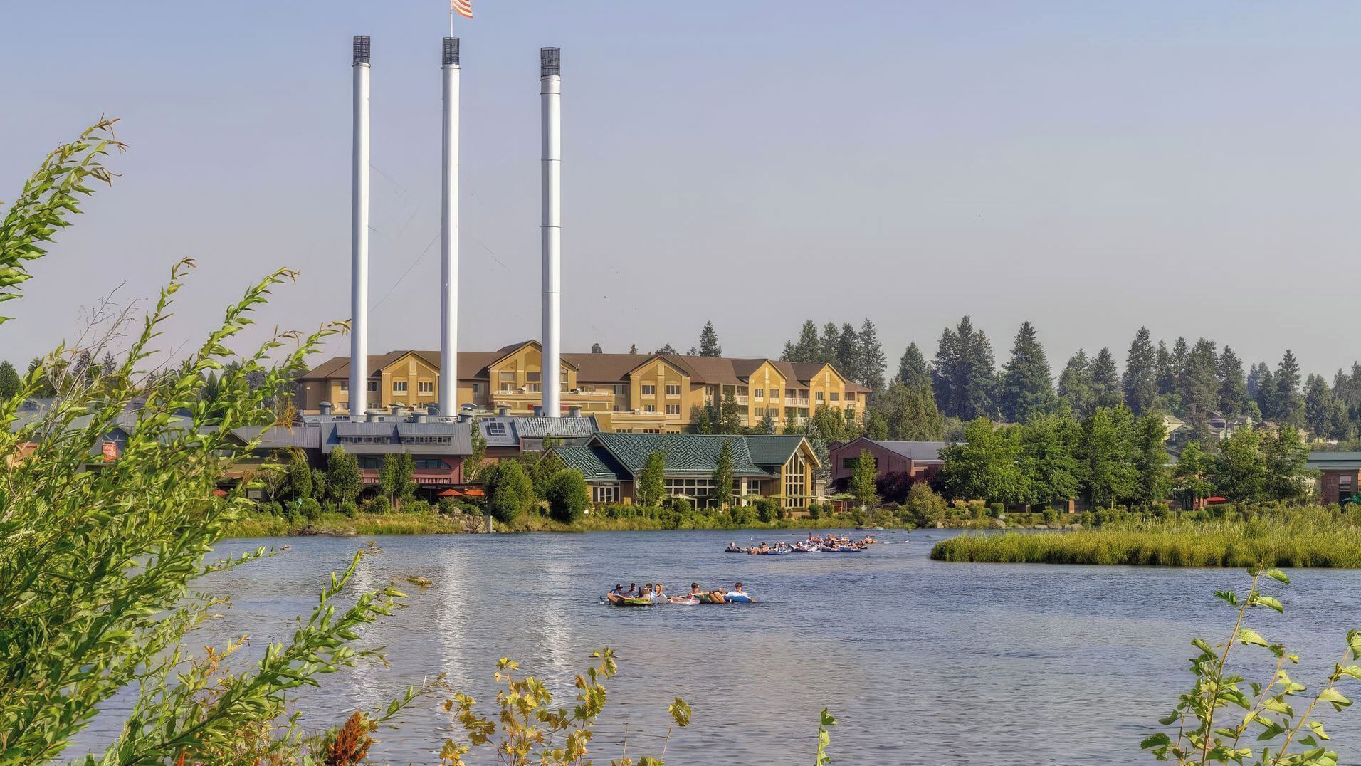 A hotel with multiple buildings, a body of water with boats, and a forested area in the background.