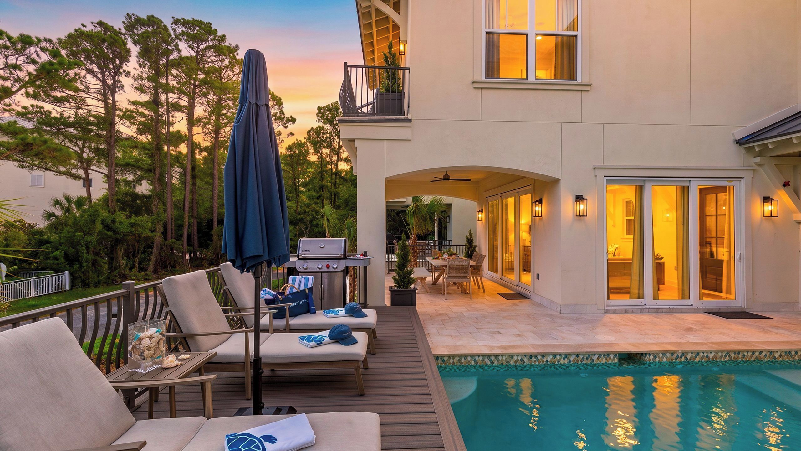 A poolside area with lounge chairs, a barbecue grill, and a view of a building with a balcony.