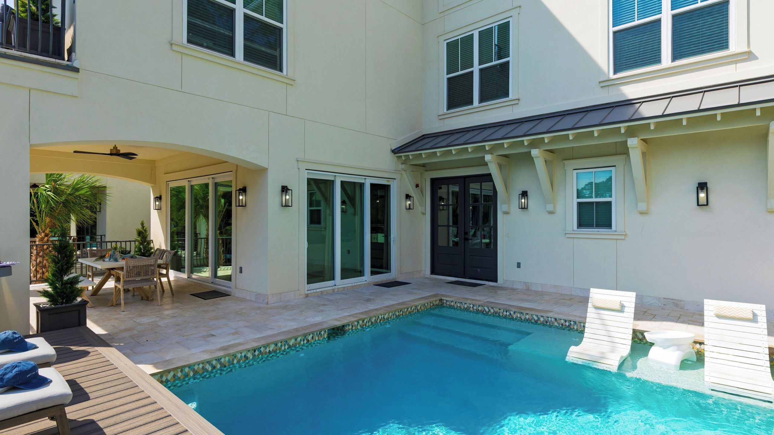 A swimming pool with a tiled deck, a covered patio area, and a door leading to a covered entryway.
