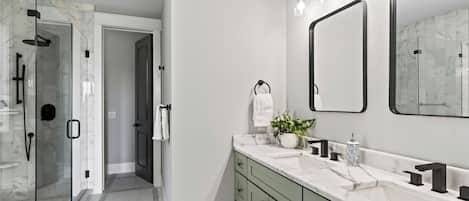 A modern bathroom with a glass-enclosed shower, a large mirror, and a marble countertop.