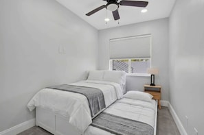 A bedroom with a bed, a nightstand, a ceiling fan, and a window with blinds. - Coveside Hideaway 5 - Coastal Escape (Deerfield Beach)