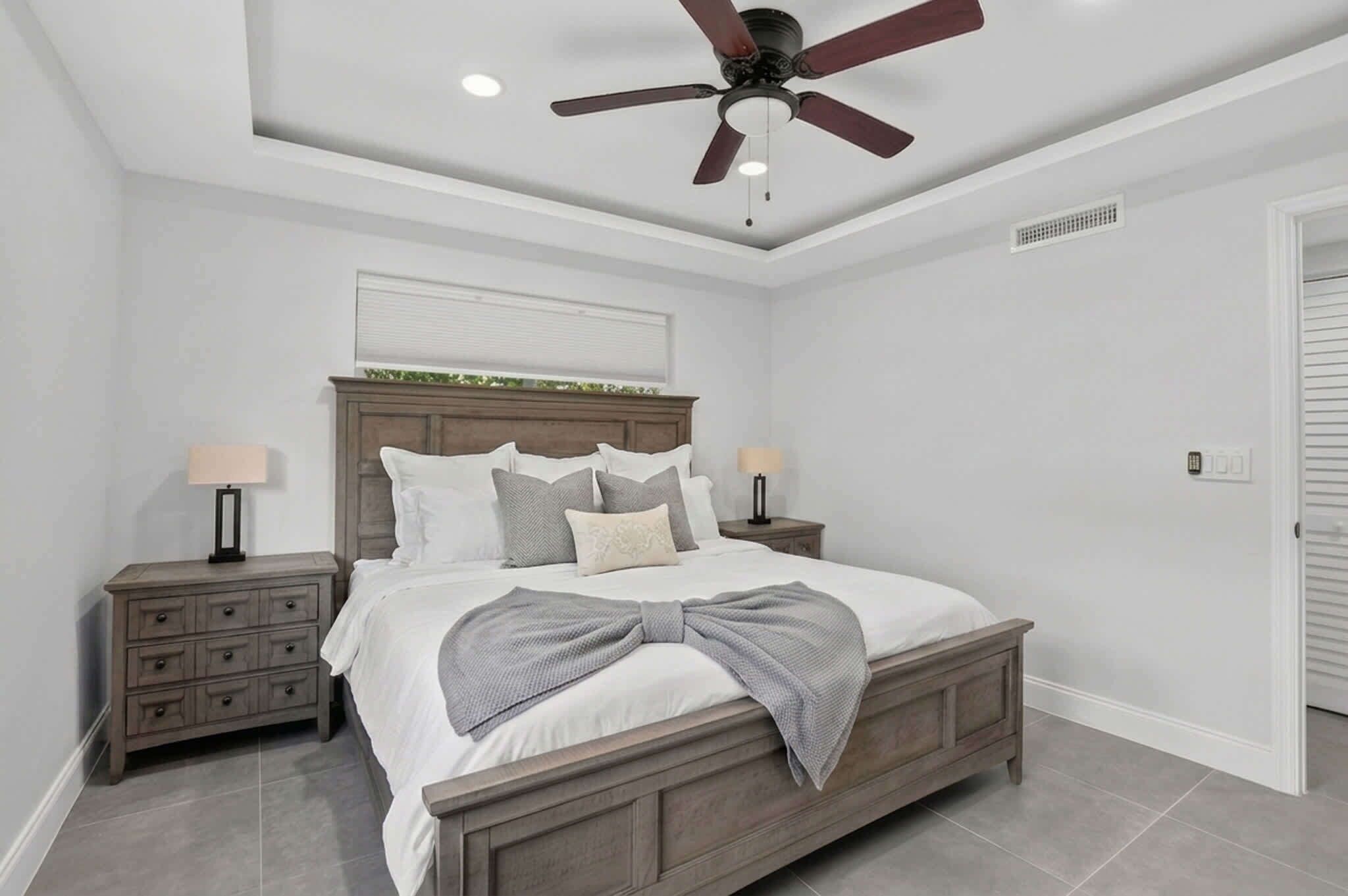 Un dormitorio con cama, mesitas de noche, ventilador de techo y una ventana con persianas.