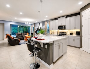 A modern kitchen with a central island, white cabinetry, and a dining area with a sofa and chairs.