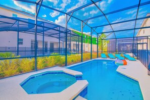 A swimming pool with a hot tub, surrounded by a glass enclosure, and blue lounge chairs.