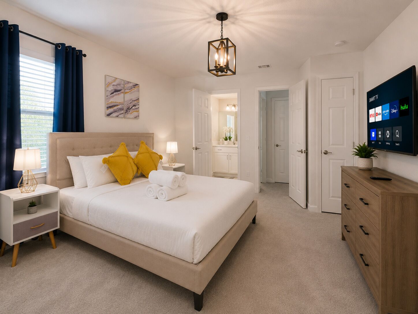 A hotel room with a bed, bedside tables, a TV, and a bathroom visible through an open door.
